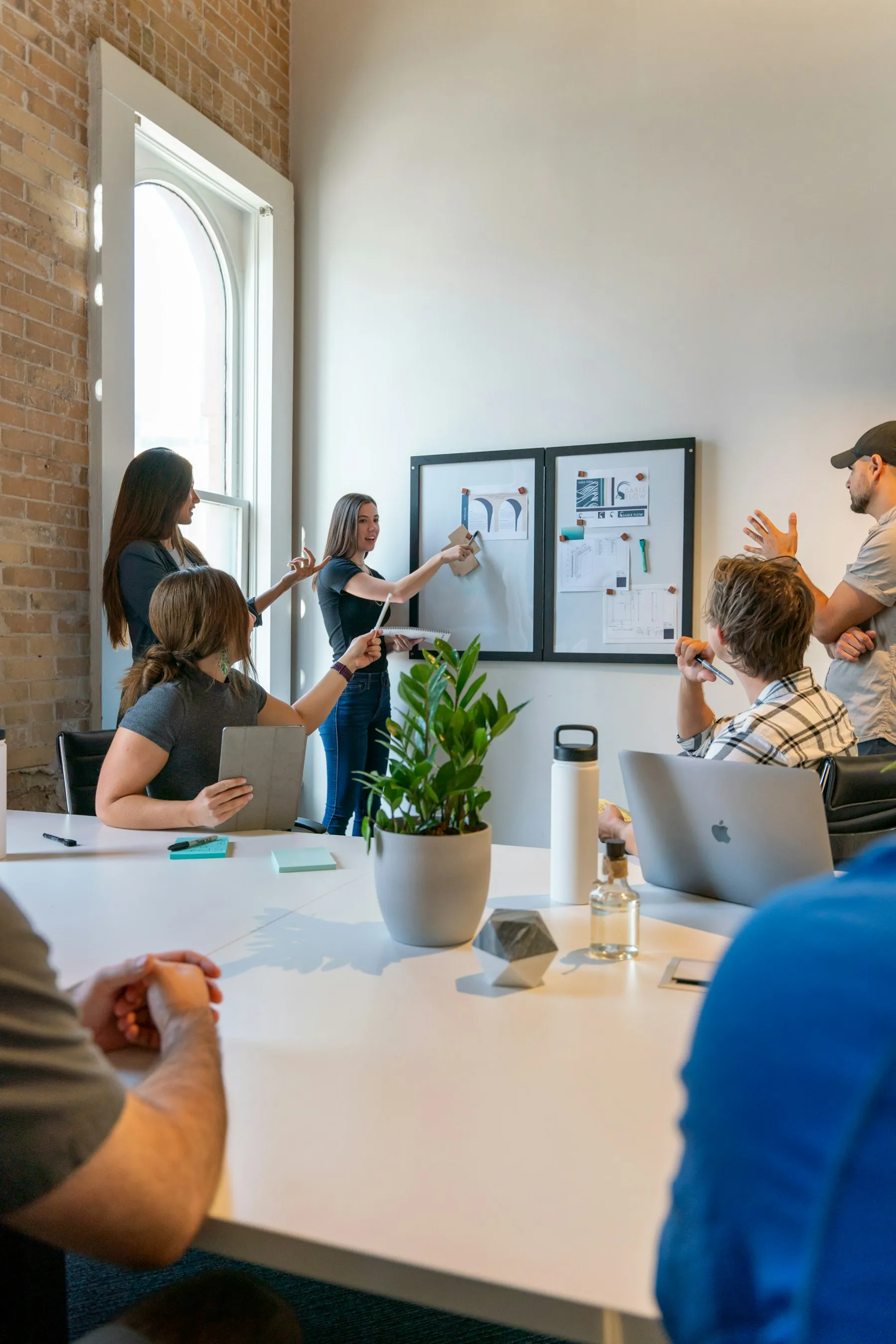 Equipe em pé diante de um quadro branco, planejando com anotações e esquemas.