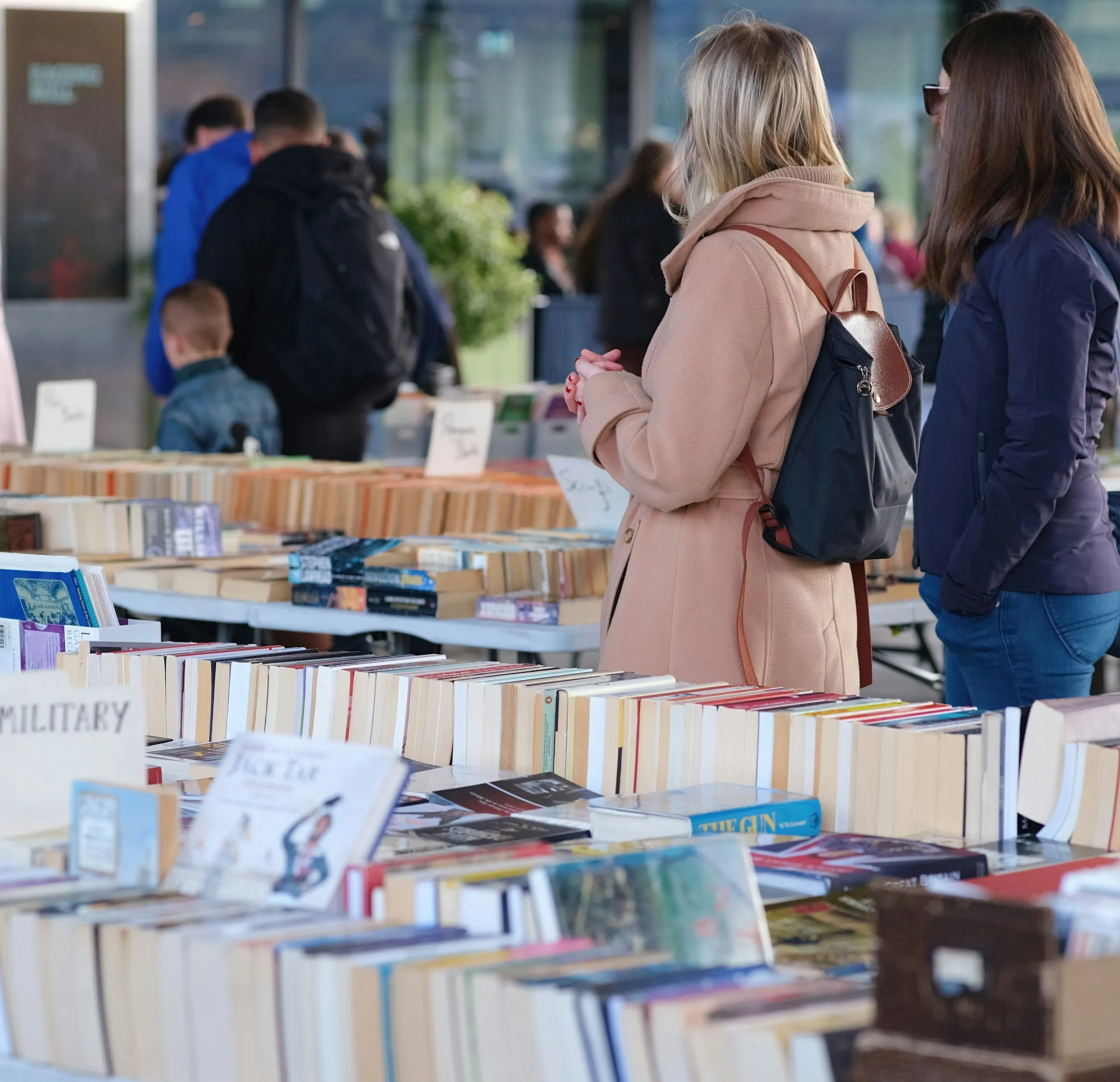 Visitantes escolhem livros em um estande de feira, entre fileiras de exemplares.
